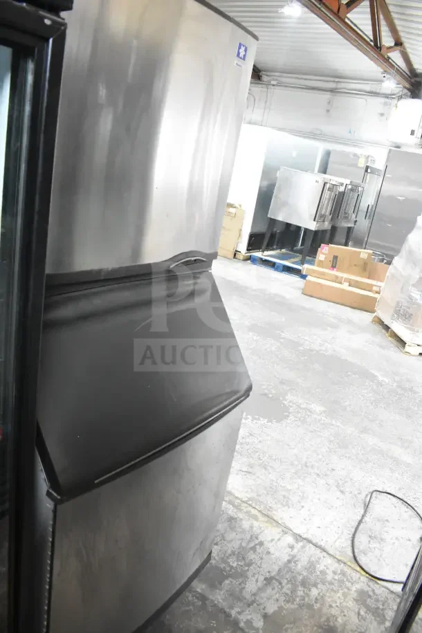 Manitowoc SY0874C commercial ice machine head on a bin, stainless steel finish, used, in a warehouse setting.