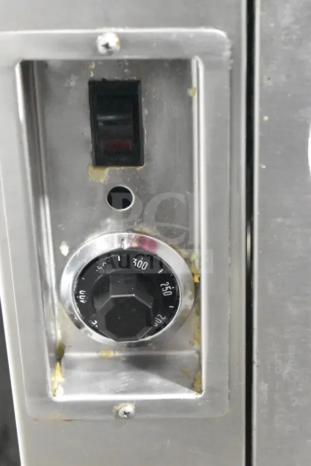 Close-up of a commercial floor-style donut fryer's control panel with temperature dial and switch. Features signs of use.