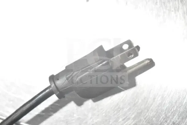 Wega espresso grinder power plug, 110 volts, showing a black, three-prong plug on a metallic surface.