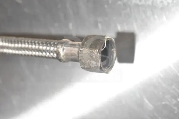 Close-up image of a damaged metal connector on a flexible hose.