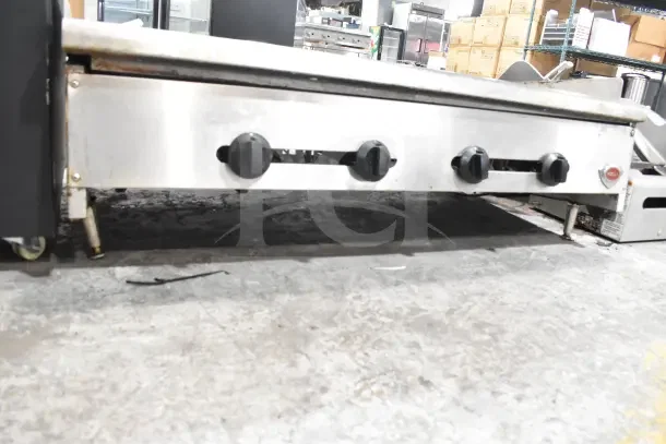 Wells Commercial Gas Griddle with four control knobs, stainless steel body, in used condition on a warehouse floor.