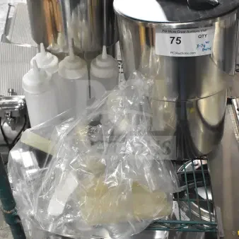 Seven stainless steel condiment bottles and pumps on a shelf. Includes plastic bottles. Auction label visible, lot 75.