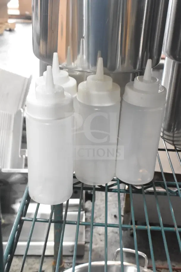 7 white plastic condiment bottles with spout caps on metal shelving; good condition, ideal for kitchen use.