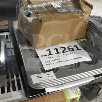 Nine scratch and dent items including a Chicago Metallic 15-cup jumbo muffin pan, wide rim pizza pan, and tapered edge blue carbon steel sheet pan. Tags show item numbers and auction details.