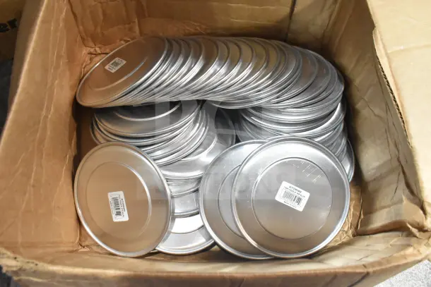 Cardboard box filled with aluminum wide rim pizza pans, each with a barcode label. Brand new, scratch and dent condition.