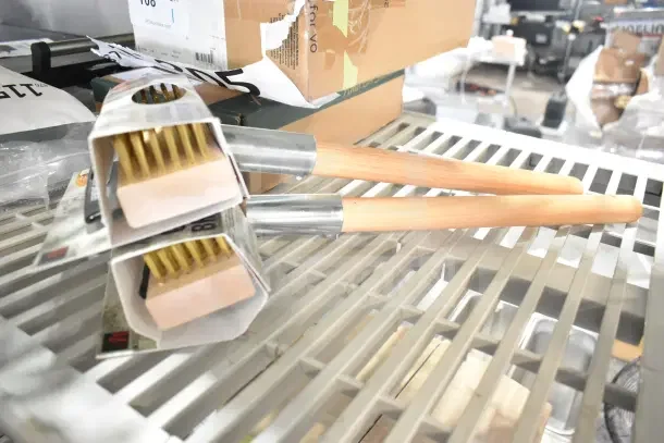 2 new Malish UGB Ultimate Grill Brushes, scratch and dent, with wooden handles and brass bristles, on a shelf.