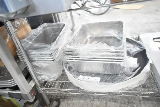 17 new scratch and dent items, including stainless steel drop-in bins and 18" black non-skid trays, wrapped in plastic.