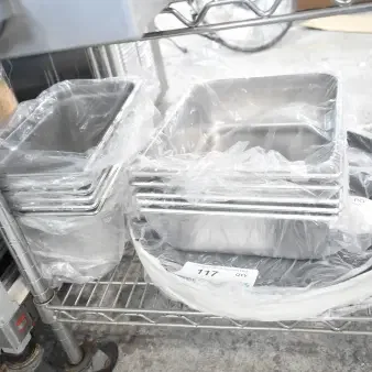 17 new scratch and dent items, including stainless steel drop-in bins and 18" black non-skid trays, wrapped in plastic.
