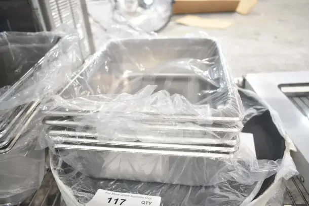 Stack of brand new stainless steel drop-in bins wrapped in plastic, auction item tag "117" visible.