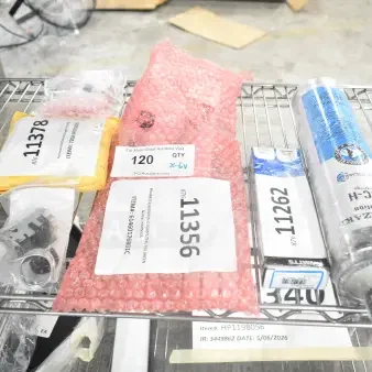 Six brand new scratch-and-dent items on a shelf, including Scotsman auger bearing, Pitco computer, Hatco valve, Hoshizaki filter, True temperature control kit, Henny Penny control. Various packaging with visible auction labels.