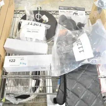 Assorted brand new scratch and dent auction items on a shelf, including a Lavex UV insect zapper bulb, Hobart sharpener assembly, Southbend timer, Outset oven mitt, and suction cup feet for cutters.