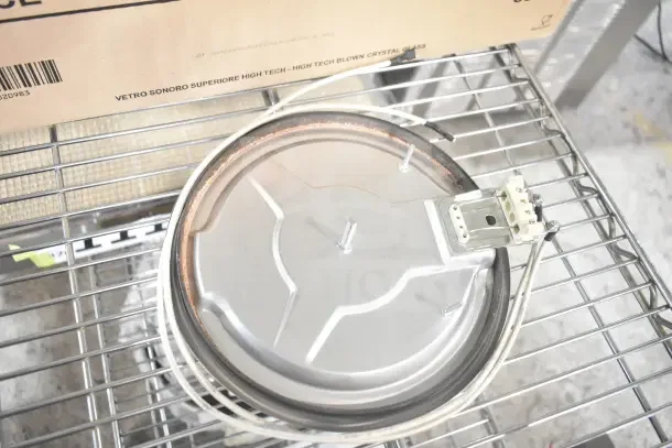 Metal component on a wire shelf with attached wiring and part exposed. Box above labeled "Vetro Sonoro Superiore High Tech."