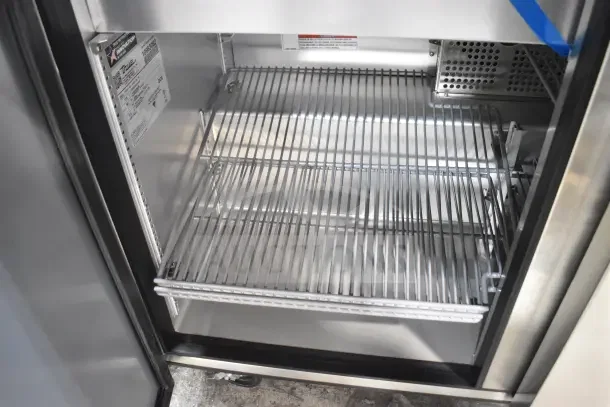 Brand new True TUC-48-HC sandwich salad prep table interior view, showing wire racks and manufacturer's label.