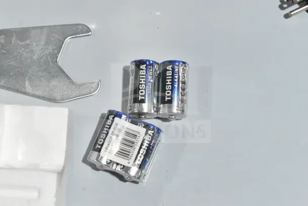 Toshiba C size batteries near a metal tool, wrapped in plastic with barcode, on a table.