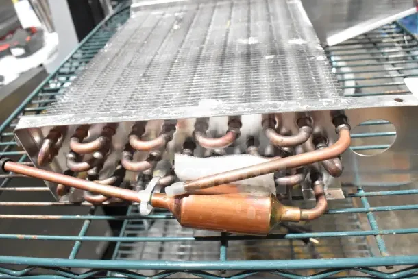Brand new evaporator coil with minor scratches and dents. Copper tubing and metal fins visible, ideal for HVAC systems.