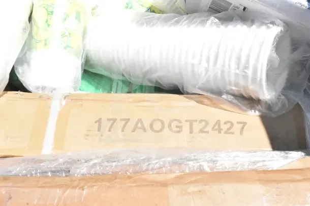 Cardboard box labeled "177AOGT2427" under plastic-wrapped items, part of a new scratch and dent auction lot.