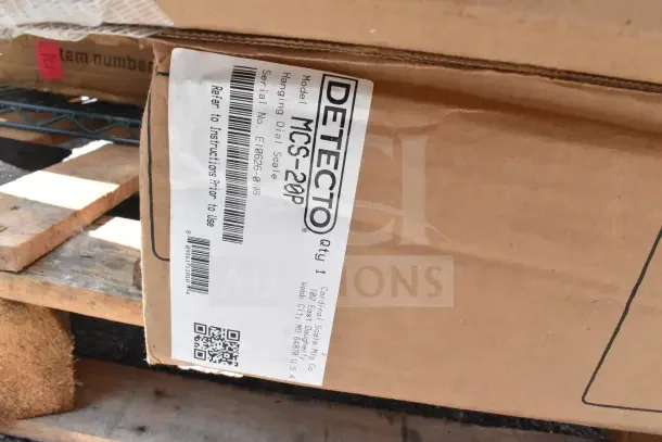 Cardboard box labeled "DETECTO MCS-20P Hanging Dial Scale" on a pallet, showing model, serial number, and origin details.