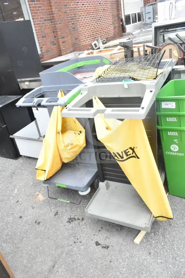Two new Lavex janitorial carts with minor scratches. Equipped with yellow bags, shelves, and wheels. Durable for cleaning tasks.