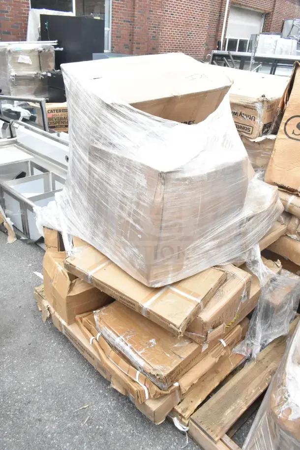 Stack of cardboard boxes containing 13 brand new scratch and dent items, including air curtain and work table, on a wooden pallet.