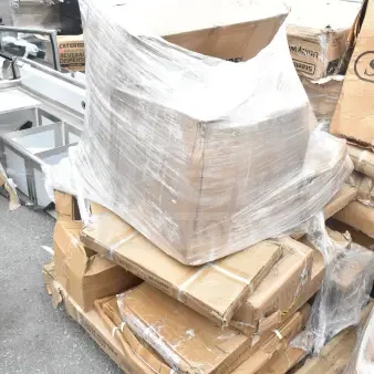 Stack of cardboard boxes containing 13 brand new scratch and dent items, including air curtain and work table, on a wooden pallet.