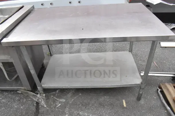 Industrial metal table with under shelf, visible wear, sturdy construction, ideal for kitchen or workshop use.
