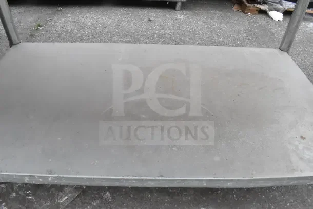 Metal table with under shelf, worn surface, sturdy construction. Ideal for industrial use, dimensions unspecified.