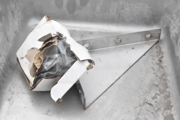 Cardboard box containing brackets and plastic, inside a metal pan. Condition appears used.