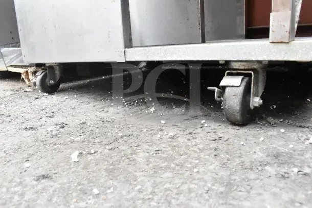 Stainless steel cart with overhead shelf on commercial casters, showing wear, ideal for heavy-duty use.