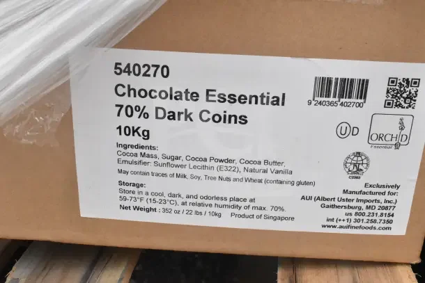 Box labeled "Chocolate Essential 70% Dark Coins" 10kg, includes ingredients like cocoa mass, sugar, and vanilla.