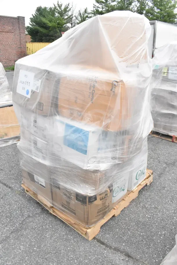 A plastic-wrapped pallet of assorted brand new but scratched or dented items including containers, forks, napkins, trash bags, and gloves.