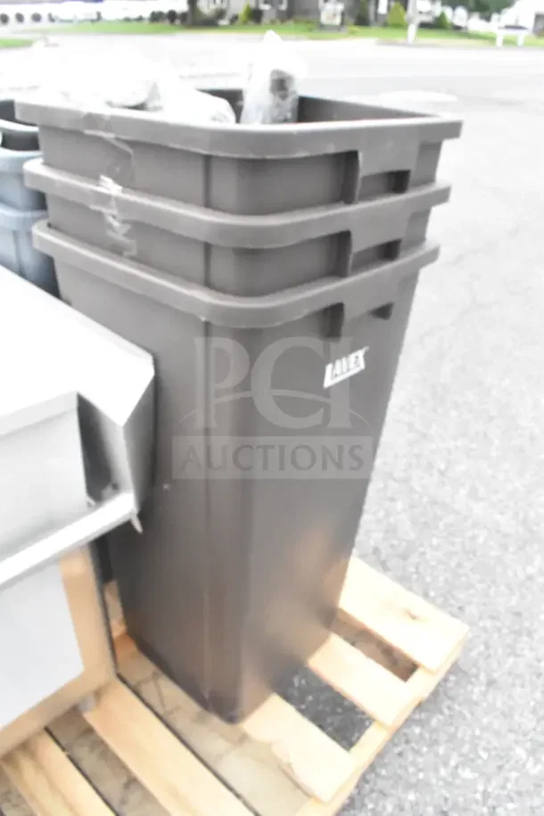 Stack of three brand new black trash cans, labeled "Landex," on a wooden pallet. Some surface scratches visible.