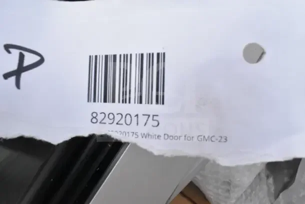 Barcode label showing "82920175" and text "White Door for GMC-23," torn paper edge and partial black item visible.