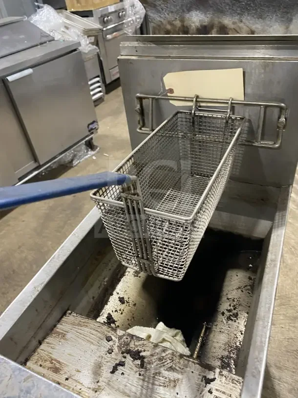 Frymaster commercial gas fryer with basket, backsplash, and hanger on casters. Used condition with visible residue.