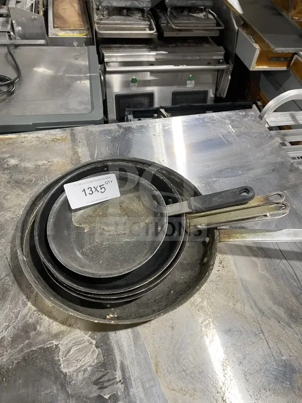 Commercial stainless steel non-stick frying pans with heavy-duty handles. Includes multiple sizes. Condition: Used. Label reads "13X5 QTY."