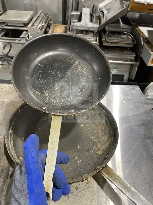 Commercial non-stick frying pans, stainless steel, heavy-duty handle, used condition with visible wear and scratches.