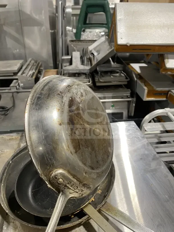 Commercial stainless steel non-stick frying pan with heavy-duty handle, visible wear. Markings indicate brand authenticity.