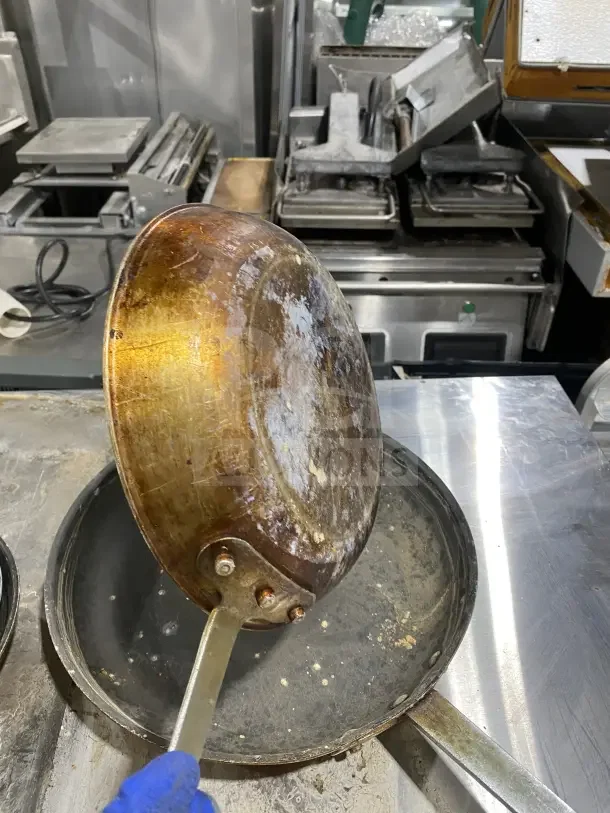 Commercial stainless steel non-stick frying pans with heavy-duty handles, used condition, minor wear visible.