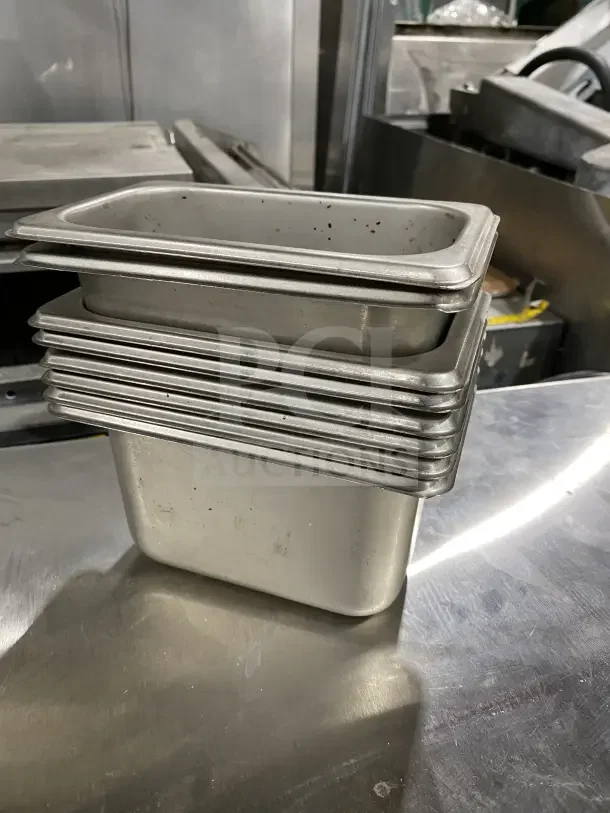 Winco commercial stainless steel trays, 8 stacked, used for salads or sauces. Durable, foodservice quality. Visible wear.