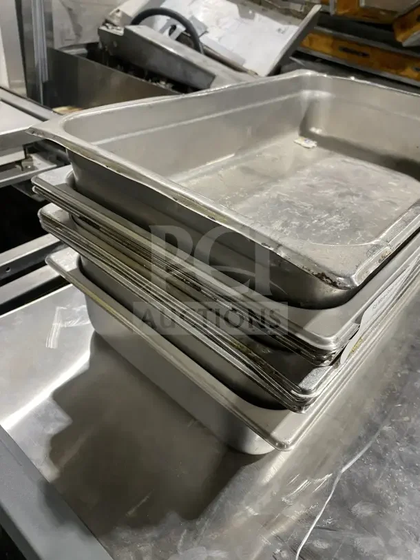 Commercial stainless steel baking trays, stack of multiple, used condition, rectangular, durable construction.