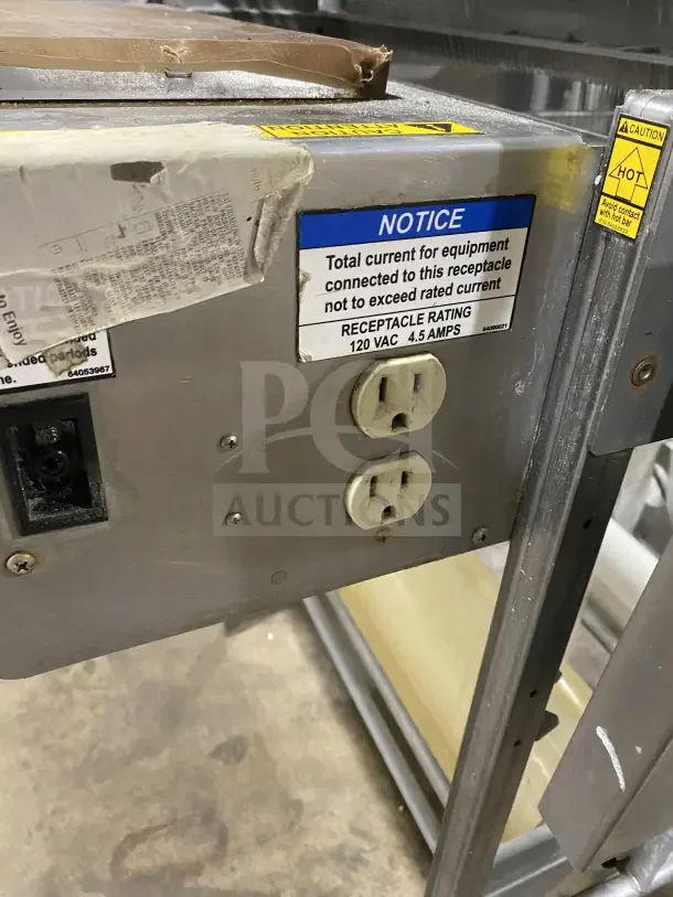 Good Nature commercial stainless steel wrapping station on casters, features electrical outlets, caution and notice labels visible.