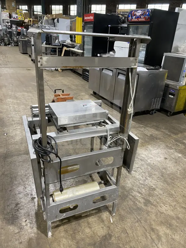 Commercial stainless steel floor-model wrapping station, Model 0662, on casters and legs. Features 120V power, includes roll holder, with serial number 0440300007.