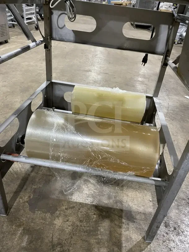 Commercial stainless steel wrapping station, Model 0662, on casters. Features film rollers, 120V power. Good condition.