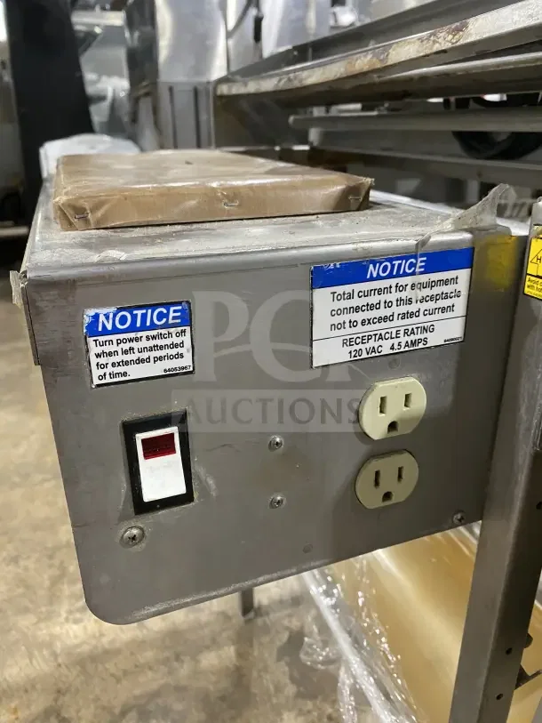 Commercial stainless steel floor-model wrapping station, model 0662, on casters and legs. Features 120V power rating, outlets, and switch with caution labels for safety.