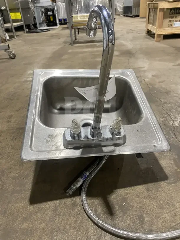 Commercial stainless steel drop-in hand sink with faucet, featuring a polished finish and two installation hoses. Slight wear visible.