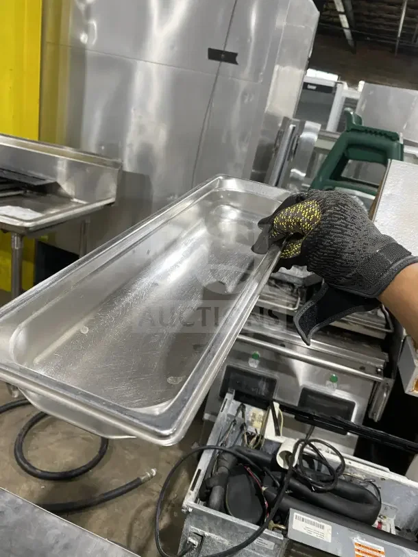 Commercial stainless steel full-size hotel pan, slightly used, held by gloved hand. Ideal for food service.