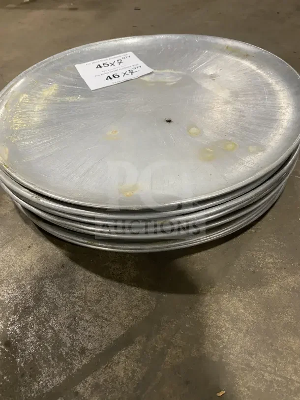 Stack of commercial round aluminum pizza pans, slightly worn, with visible markings; includes label noting quantity.