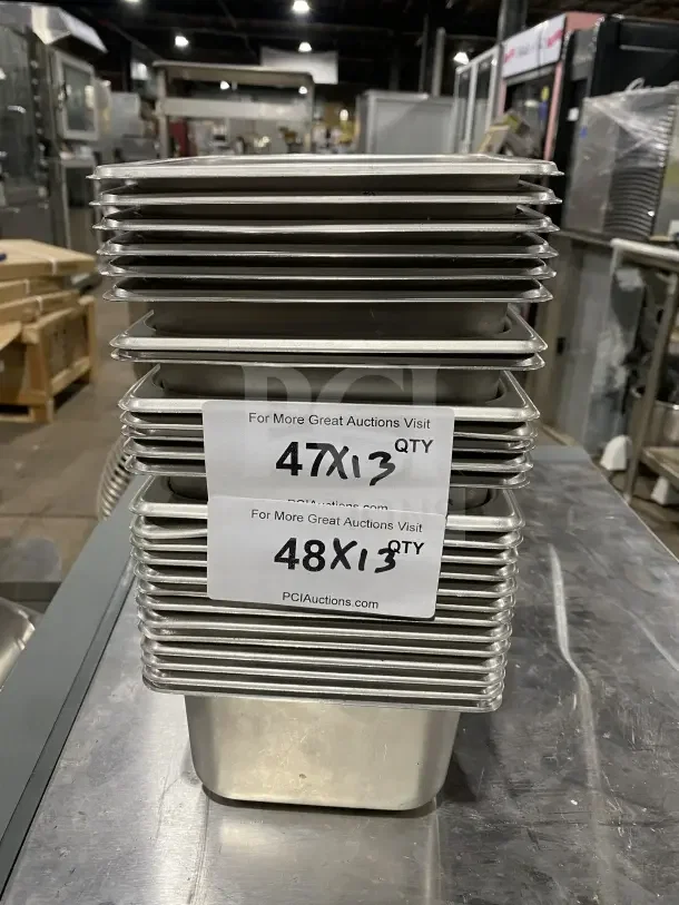 Stack of stainless steel sixth-size food pans, unused, with quantity labels showing "47x13" and "48x13."