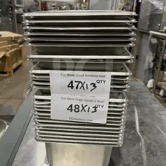 Stack of stainless steel sixth-size food pans, new condition. Labels indicate auction info: "47X13 QTY" and "48X13 QTY."
