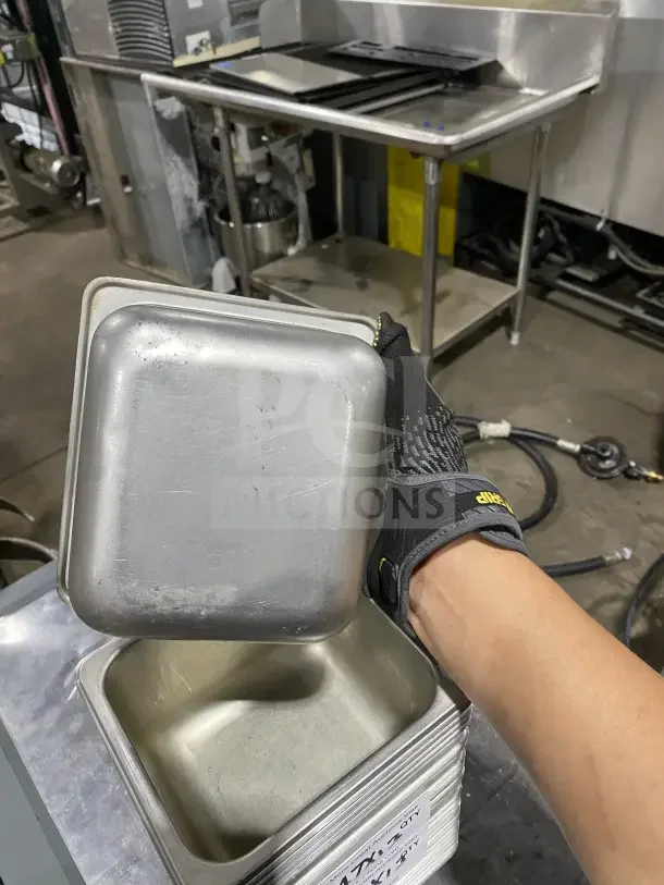 Commercial stainless steel sixth-size food pan, used condition, visible wear. Dimensions: 13X. Stack of similar pans nearby.