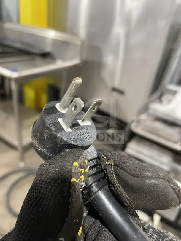Close-up of a power plug held by a gloved hand, with focus on plug prongs and visible "Zhejiang Yonggian" marking.